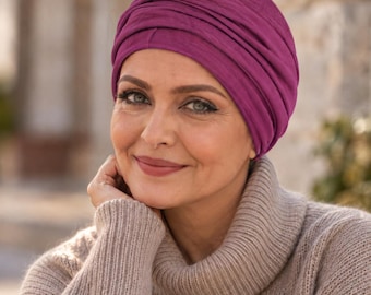 May include: A deep magenta turban-style head covering featuring multiple horizontal fabric folds and a smooth, fitted base. The headwear is crafted from a soft, jersey-like material that wraps around the head to create a layered, ruched appearance.