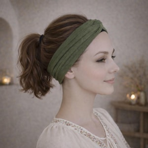 Könnte beinhalten: Ein grünes Stirnband mit Knoten aus weichem Stoff. Das Stirnband wird von einer Person mit braunen Haaren getragen, die zu einem Pferdeschwanz gebunden sind. Die Person trägt eine cremefarbene Bluse.