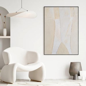 Könnte beinhalten: Abstrakter Kunstdruck mit beige und weißen geometrischen Formen in einem schwarzen Rahmen. Der Druck hängt an einer weißen Wand über einem weißen Sessel.