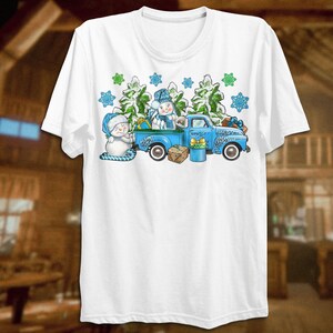 May include: A white t-shirt with a blue pickup truck carrying two snowmen and a Christmas tree. The truck is decorated with snowflakes and green pine branches.