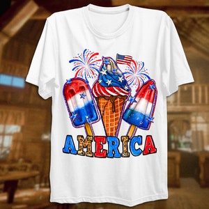 May include: White t-shirt featuring a red, white and blue ice cream cone, popsicles, and fireworks graphic. The text "AMERICA" is printed in red, white and blue with a leopard print pattern.