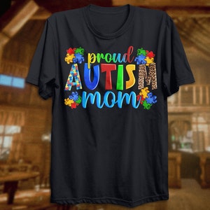 Może przedstawiać: Czarny T-shirt z napisem "proud autism mom" w kolorach tęczy z puzzlami i wzorem lamparta.