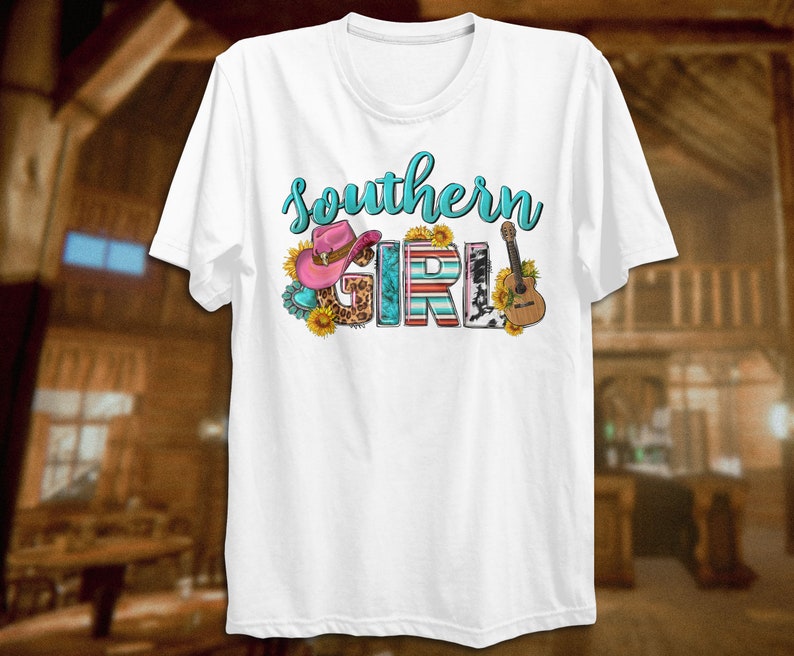 May include: White t-shirt with the text "Southern Girl" in turquoise blue letters. The letters are decorated with a pink cowboy hat, sunflowers, a guitar, and a cow print.