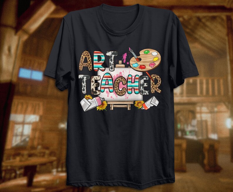 May include: Black t-shirt with the text "Art Teacher" in colorful letters with a paintbrush, paint splatters, and a paint palette on a canvas.