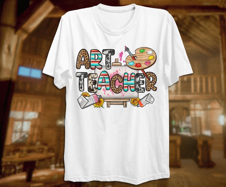 May include: White t-shirt with the text "ART TEACHER" in colorful letters with a paint palette and paintbrushes. The letters have a leopard print and striped pattern.