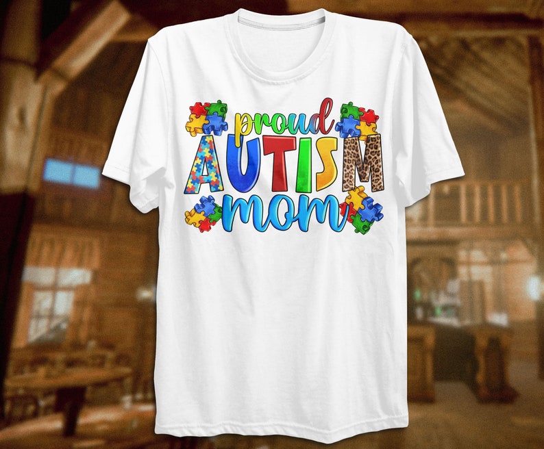 Może przedstawiać: Biała koszulka z napisem "proud autism mom" w kolorowych literach otoczonych puzzlami. Słowo "autism" jest w kolorze czerwonym, ż&oacute;łtym, niebieskim i zielonym. Elementy puzzli są niebieskie, czerwone, ż&oacute;łte i zielone. Słowo "mom" jest w kolorze niebieskim i zielonym. Za słowem "autism" znajduje się wz&oacute;r w panterkę.