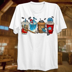 May include: White t-shirt with a graphic of four different iced coffee drinks with hockey equipment, including a hockey stick, puck, and helmet.