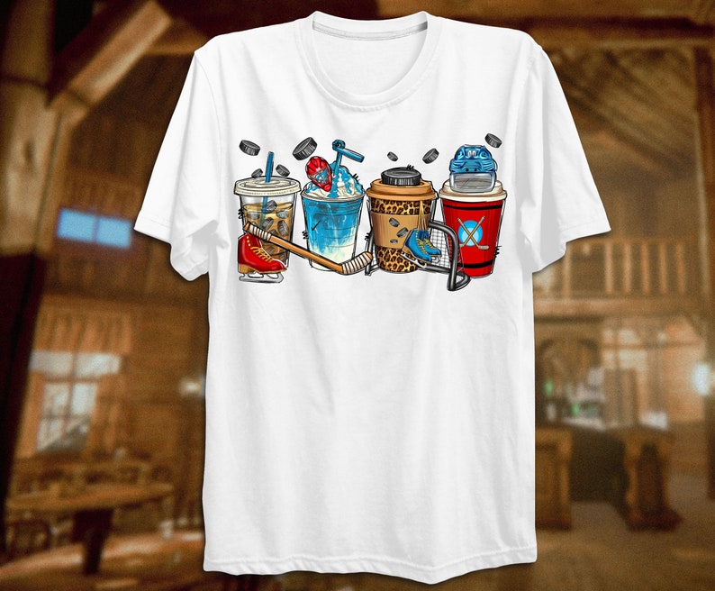 May include: White t-shirt with a graphic of four different iced coffee drinks with hockey equipment, including a hockey stick, puck, and helmet.