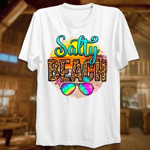May include: White t-shirt with a graphic of a sunset with a leopard print design and the text "Salty Beach". Sunglasses are in front of the sunset.