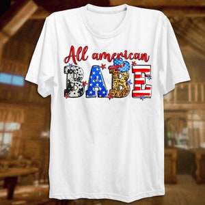 May include: White t-shirt with the text "All American Babe" in red, blue, and white letters. The letters are decorated with stars, cow print, leopard print, and an American flag.