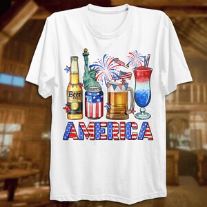 May include: White t-shirt with a red, white, and blue American flag design. The design features a beer bottle, a can of beer, a beer mug, a cocktail, and fireworks. The text "AMERICA" is written in red, white, and blue letters.