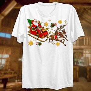 Puede incluir: Camiseta blanca con un dise&ntilde;o navide&ntilde;o que presenta a Pap&aacute; Noel en un trineo rojo tirado por dos renos. El dise&ntilde;o incluye estrellas doradas, bastones de caramelo y acebo.