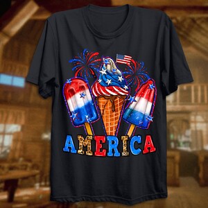 May include: A black t-shirt featuring a graphic of ice cream cones and popsicles decorated in red, white and blue. The graphic also includes fireworks and a small American flag. The text "AMERICA" is printed below the graphic in a leopard print font.