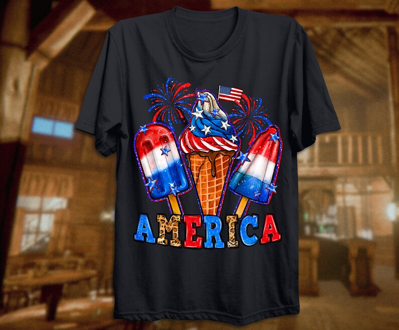 May include: A black t-shirt featuring a graphic of ice cream cones and popsicles decorated in red, white and blue. The graphic also includes fireworks and a small American flag. The text "AMERICA" is printed below the graphic in a leopard print font.