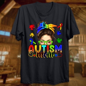 May include: Black t-shirt with a colorful graphic of a woman with a bun and glasses. The graphic includes puzzle pieces and the text "Autism Mom".