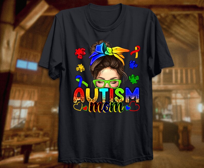 May include: Black t-shirt with a colorful graphic of a woman with a bun and glasses. The graphic includes puzzle pieces and the text "Autism Mom".