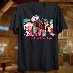 May include: Black t-shirt with a colorful graphic design that says "LPN" with a stethoscope, pills, a nurse's hat, and a pair of pink clogs. The text below the graphic says "Licensed Practical Nurse".