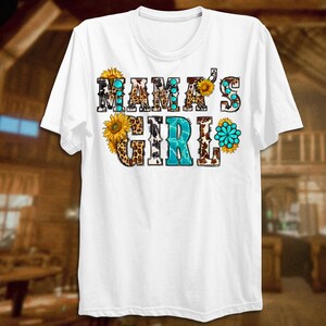 May include: White t-shirt with the text "Mama's Girl" in colorful letters with a cowhide, leopard print, and sunflower design.