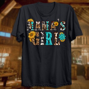 May include: A dark blue t-shirt with the text "Mama's Girl" in white letters. The text is decorated with a pattern of sunflowers, leopard print, and cow print.