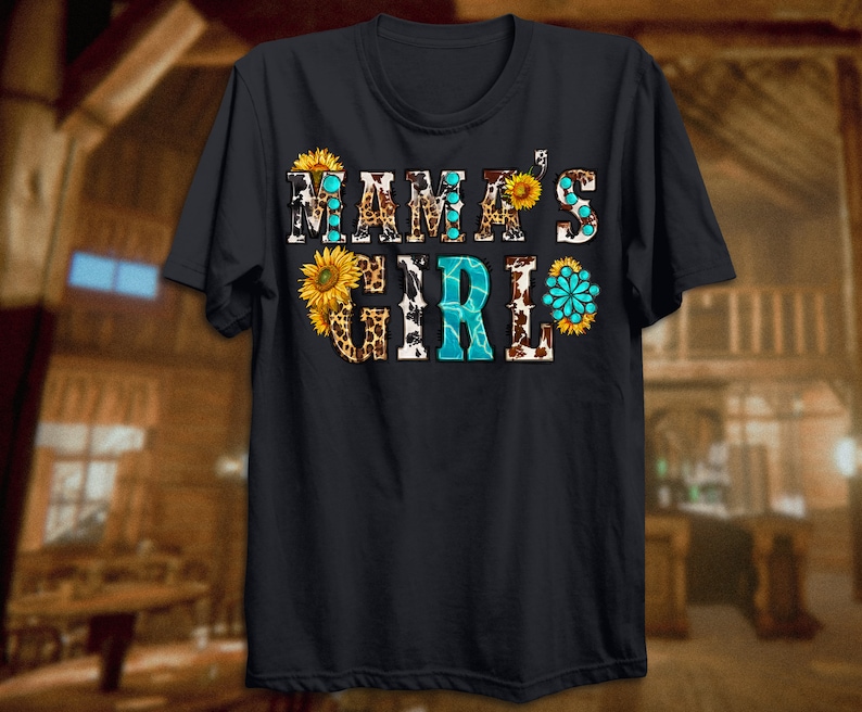 May include: A dark blue t-shirt with the text "Mama's Girl" in white letters. The text is decorated with a pattern of sunflowers, leopard print, and cow print.