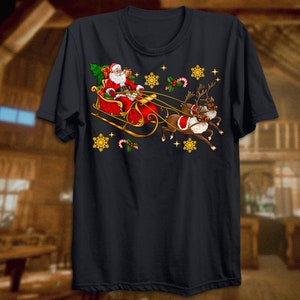 Puede incluir: Una camiseta negra con un dise&ntilde;o navide&ntilde;o que presenta a Pap&aacute; Noel en un trineo tirado por renos. El dise&ntilde;o incluye copos de nieve, bastones de caramelo y acebo.