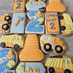 Könnte beinhalten: Dekorierte Kekse zum Thema Bau. Die Kekse zeigen Straßenschilder mit "SPEED LIMIT 2", Leitkegel, Lastwagen und einen Keks mit dem Namen "Livio". Die Kekse sind mit orangefarbenem, gelbem, blauem und schwarzem Zuckerguss verziert.