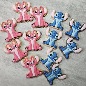Peut inclure: Une collection de biscuits au sucre décorés en forme des personnages Stitch et Angel du film d'animation Lilo & Stitch. Les biscuits sont roses et bleus avec des détails blancs et noirs.