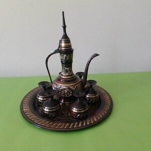 May include: A brass tea set with a decorative tray. The set includes a teapot with a tall spout and six small cups.