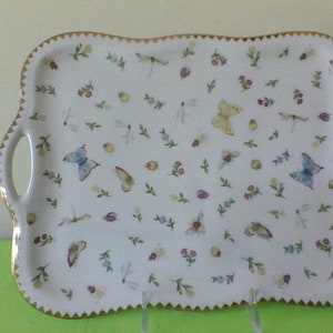 May include: White ceramic serving tray with a gold rim and a scalloped edge. The tray is decorated with a pattern of butterflies, dragonflies, and flowers.