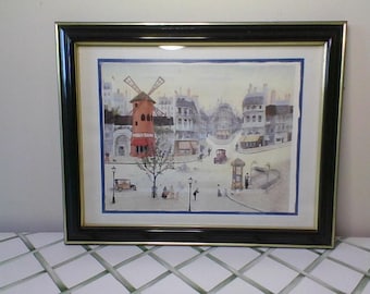 May include: A framed watercolor painting depicting a Parisian street scene with a red windmill building and a blue sky. The painting is in a black frame with a gold trim.