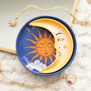 May include: A blue and yellow ceramic dish featuring a crescent moon design and a sun with a closed eye. The dish is ideal for storing jewellery or other small items.