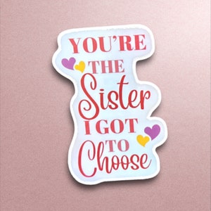 May include: White sticker with pink and yellow hearts and the text "You're the sister I got to choose."