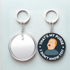 May include: Two keychains, one blank and one with a cartoon image of a character with the text "THAT'S MY PURSE I DON'T KNOW YOU" in white lettering on a dark blue background. Both keychains have a silver ring and chain.