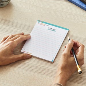 以下が含まれることがあります： 青い白の罫線入りのメモ帳。メモ帳の上部に「From the desk of Edith Harrison」という文字が印刷されています。メモ帳は木製の表面の上に置かれています。