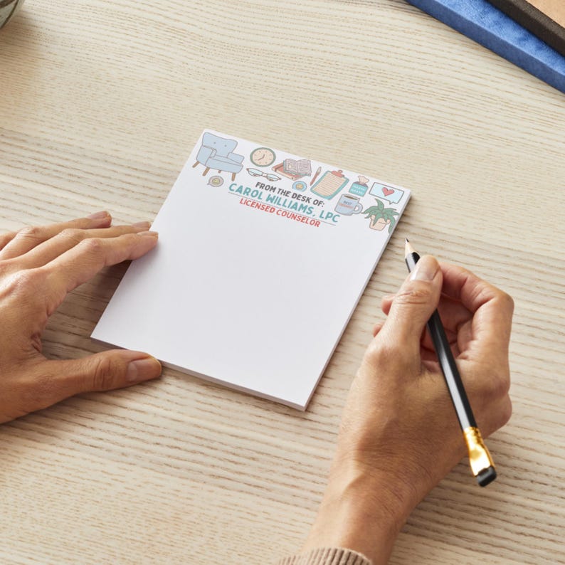 May include: A white notepad with a decorative border featuring a chair, clock, and coffee cup. The notepad reads "FROM THE DESK OF: CAROL WILLIAMS, LPC LICENSED COUNSELOR". A pencil is held over the notepad.