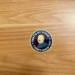 May include: A black and white sticker with a cartoon image of a man with a surprised expression. The sticker says "That's my purse, I don't know you."