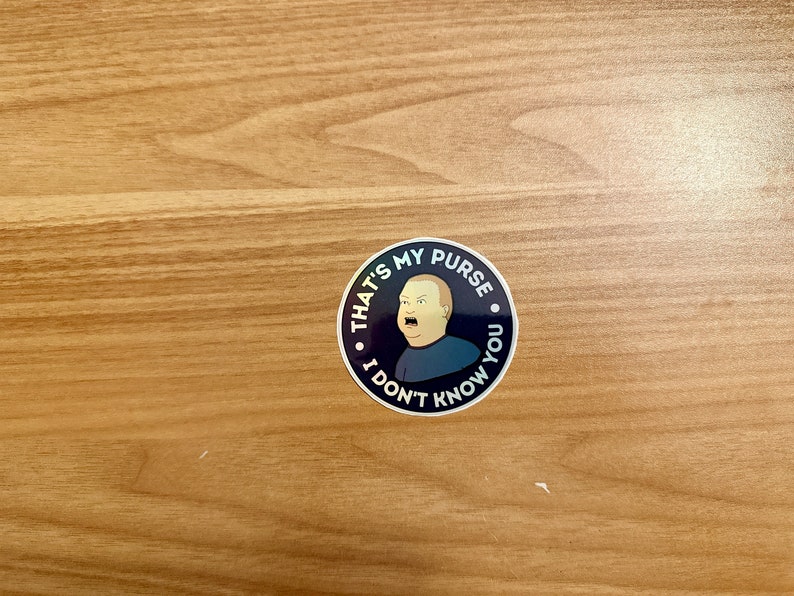 May include: A black and white sticker with a cartoon image of a man with a surprised expression. The sticker says "That's my purse, I don't know you."