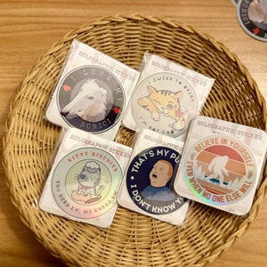 May include: Five holographic stickers with different designs. The stickers are round and feature images of a dog, a cat, a cartoon cat, a man, and a Bigfoot. The stickers have text that reads "I love my Borzoi", "I swear to drunk", "Kitty Biscuits", "That's my pu", and "Believe in yourself".