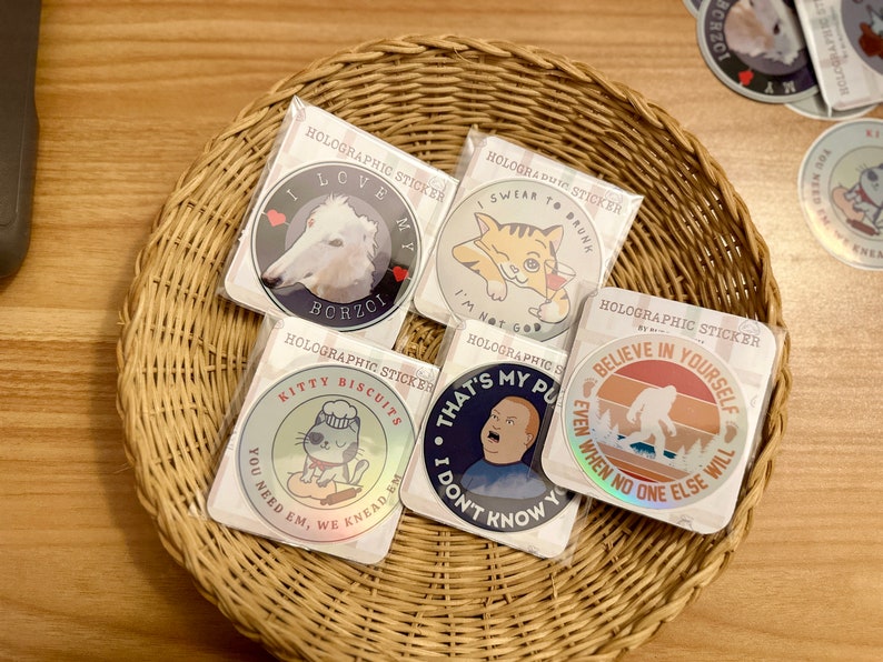 May include: Five holographic stickers with different designs. The stickers are round and feature images of a dog, a cat, a cartoon cat, a man, and a Bigfoot. The stickers have text that reads "I love my Borzoi", "I swear to drunk", "Kitty Biscuits", "That's my pu", and "Believe in yourself".