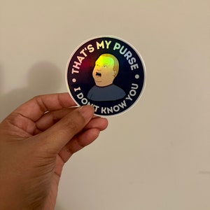May include: A round sticker with a holographic finish features a cartoon character with a surprised expression. The sticker has the text "That's my purse. I don't know you."