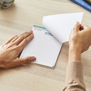 以下が含まれることがあります： 青とターコイズの縁取りが施された白い罫線入りノート。ノートの前面には「From the Desk of Edith Harrison」という文字が印刷されています。