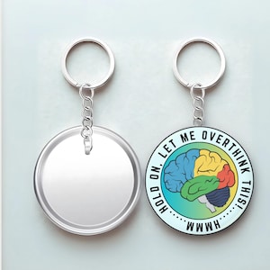 May include: Two round keychains. One is blank, the other features a colorful brain graphic with the text "HOLD ON, LET ME OVERTHINK THIS!" and "WMMH". The keychains have silver rings and chains.