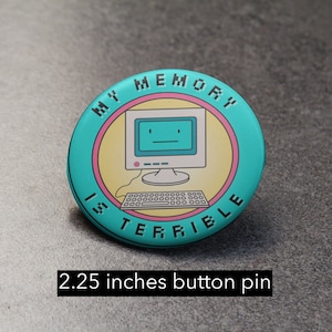 May include: A turquoise button pin with a pink and yellow circle in the center. The circle features a cartoon computer with a sad face and the text "MY MEMORY IS TERRIBLE". The pin is 2.25 inches in diameter.