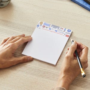 May include: A white notepad with a blue and red border featuring icons related to coding and programming. The text "console.log(editNotes)" is printed on the notepad.