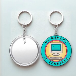 May include: Two round keychains. One is blank and silver. The other has a teal border with the words "MY MEMORY IS TERRIBLE" around a retro computer graphic. The computer has a yellow screen and a keyboard.