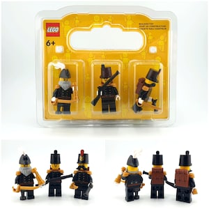 Puede incluir: Un set de construcción LEGO con tres minifiguras de soldados históricos con uniformes negros, detalles dorados, sombreros marrones y mochilas. Las figuras se presentan en un blíster de plástico transparente con un fondo de cartón amarillo.