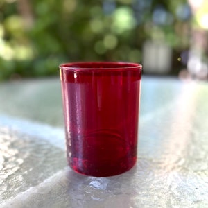 Könnte beinhalten: Ein roter Glas-Votivkerzenhalter. Der Halter ist aus klarem Glas mit einer roten Tönung.
