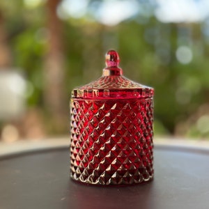 May include: A red glass jar with a diamond pattern and a lid. The jar is sitting on a gray surface.
