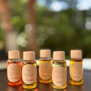 May include: Five small glass bottles with brown lids and labels. The labels are white with a black 'W' logo and the text 'Wicks & Wax Candle Supplies'. The bottles contain different colored liquids and have labels with the scents 'Ocean Breeze', 'Pumpkin', 'Vanilla Bean', 'Mango', and 'Blueberry'.