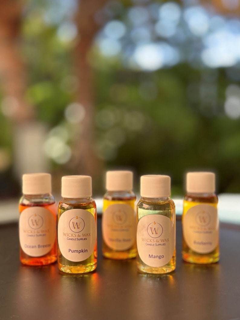 May include: Five small glass bottles with brown lids and labels. The labels are white with a black 'W' logo and the text 'Wicks & Wax Candle Supplies'. The bottles contain different colored liquids and have labels with the scents 'Ocean Breeze', 'Pumpkin', 'Vanilla Bean', 'Mango', and 'Blueberry'.